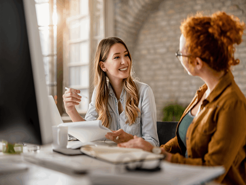 duas mulheres conversam e sorriem em escritório de trabalho com facetas dentais ou lentes de contato dental 