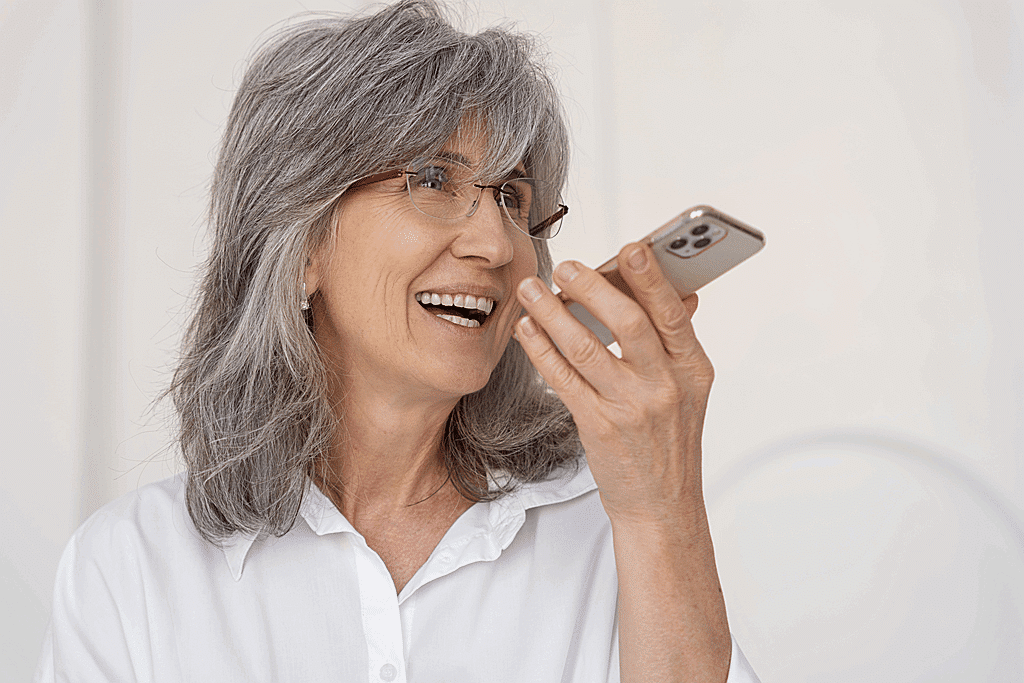 mulher idosa sorridente com implante dentario gravando mensagem de voz usando um dispositivo smartphone