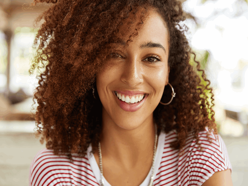 mulher negra com um sorriso largo com facetas dentais ou lentes de contato dental vestindo uma camiseta listrada olhando para a câmera 
