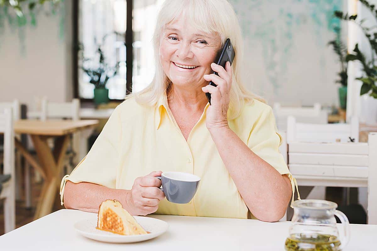 Mulher idosa sorridente fala ao telefone enquanto toma café