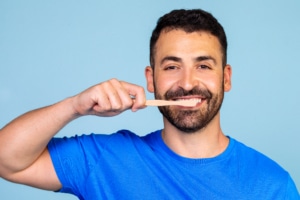 homem jovem vestindo uma camiseta azul sobre fundo azul escovando os dentes
